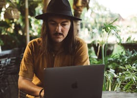 Man with a Hat Sitting in a Garden with Laptop