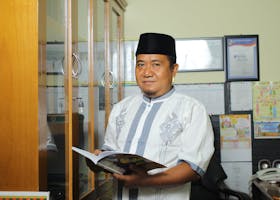 A teacher standing in an office in Indonesia, holding a book, conveying education.
